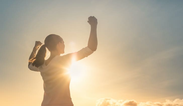 A person standing in the sun with their arms raised.