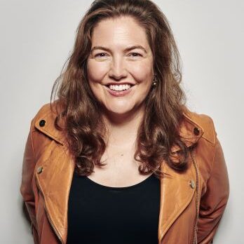 A woman in brown jacket smiling for the camera.